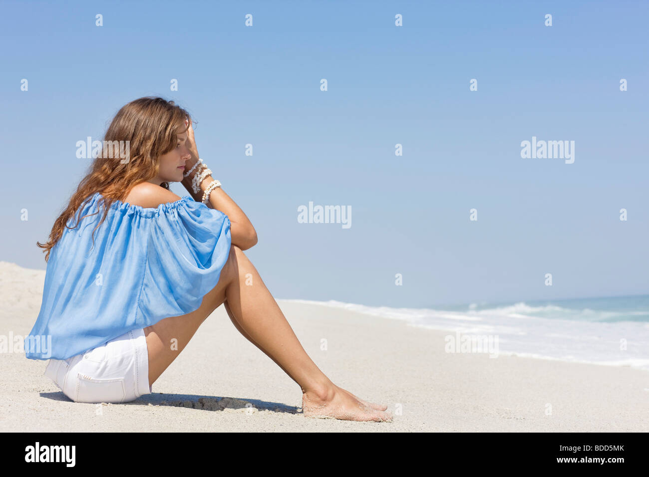 Donna seduta sulla spiaggia e di pensiero Foto stock - Alamy