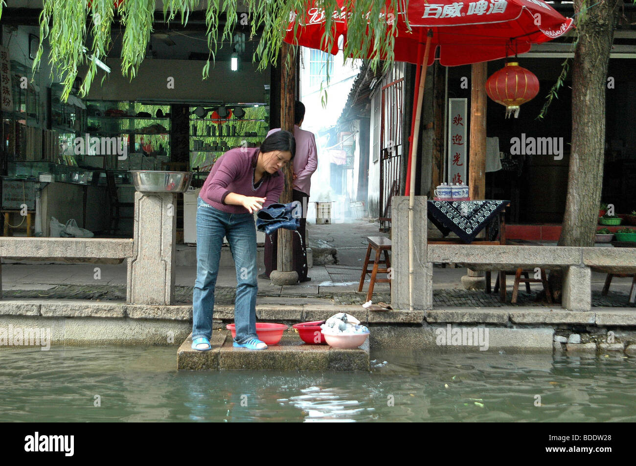 La Cina, nella provincia di Zhejiang, Wuzhen, Donna lava vestiti in fiume Foto Stock