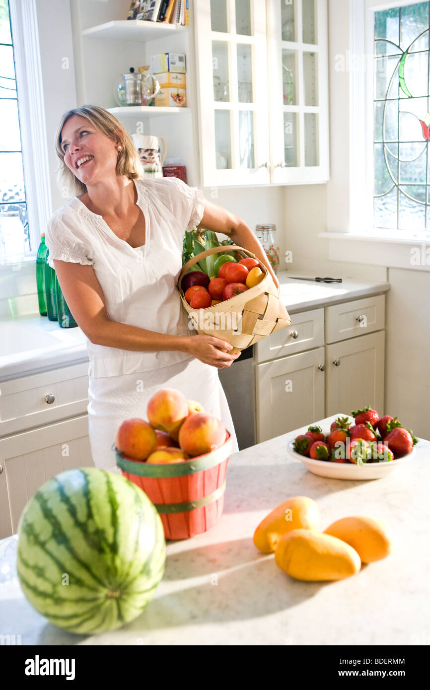 Metà donna adulta holding cesto di frutta fresca e verdura in cucina Foto Stock