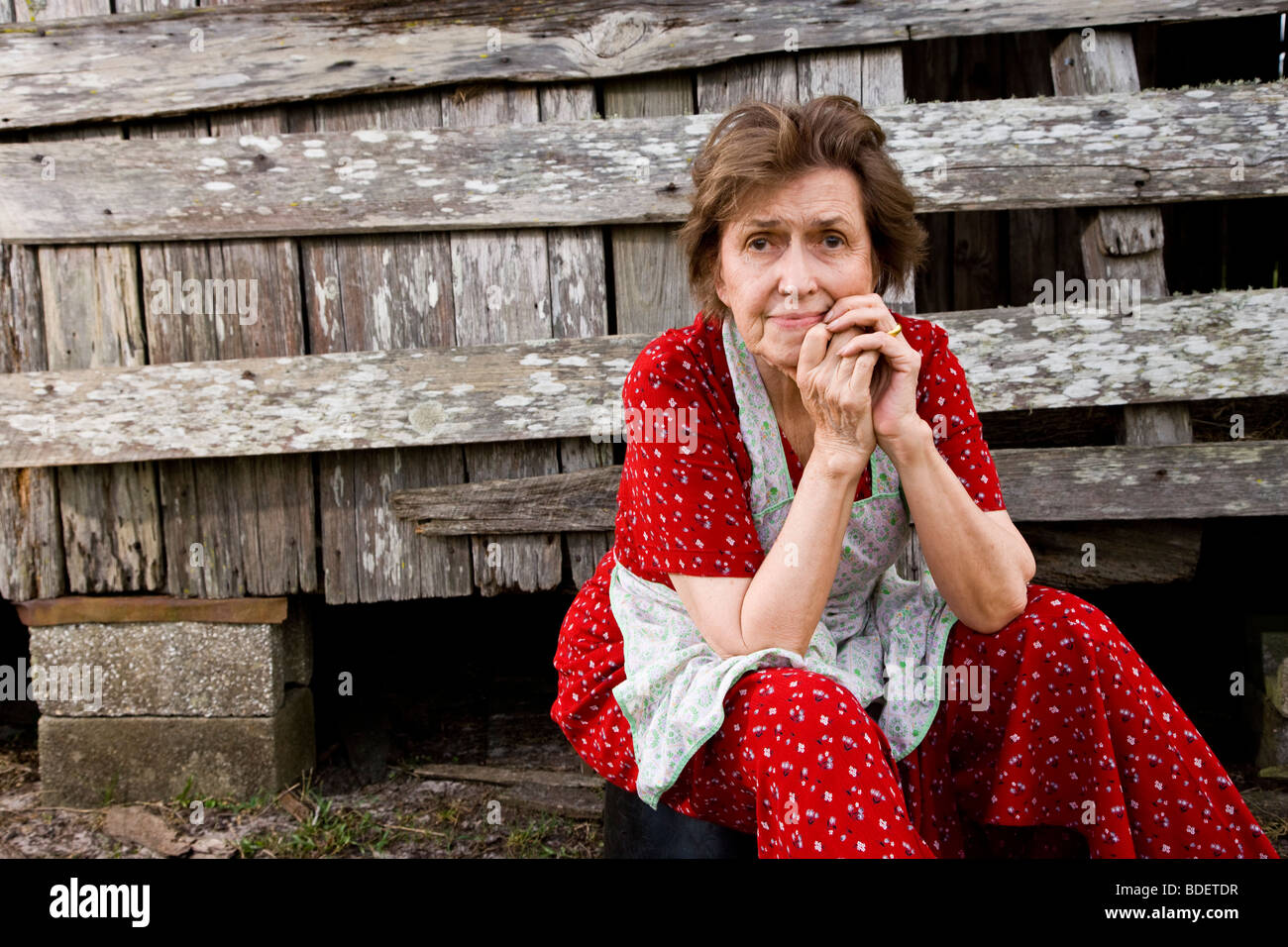 Senior donna seduta in agriturismo vicino a fienile preoccupante Foto Stock