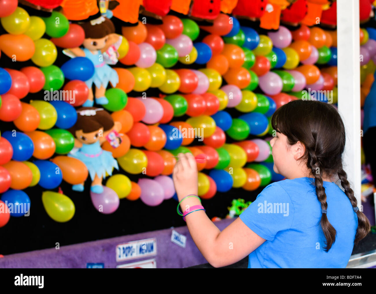 Una ragazza con trecce si prepara a lanciare un dardo in corrispondenza di una parete di palloncini alla fiera della contea. Foto Stock