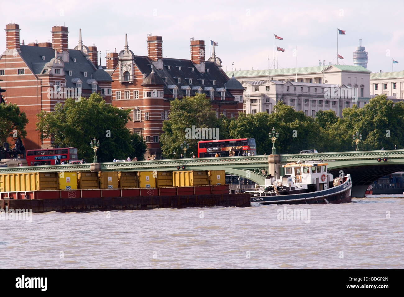 Un rimorchiatore chiatte di traino caricato con contenitori di rifiuti combattendo contro il flusso di marea del Tamigi si avvicina a Westminster Bridge Foto Stock
