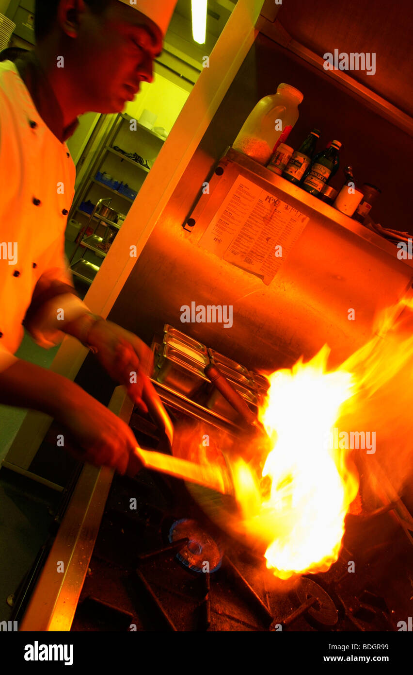 Chef indiano indossando bianchi e il cappello da cuoco di colore rosso fiamma di cottura stufa flambe antincendio Foto Stock