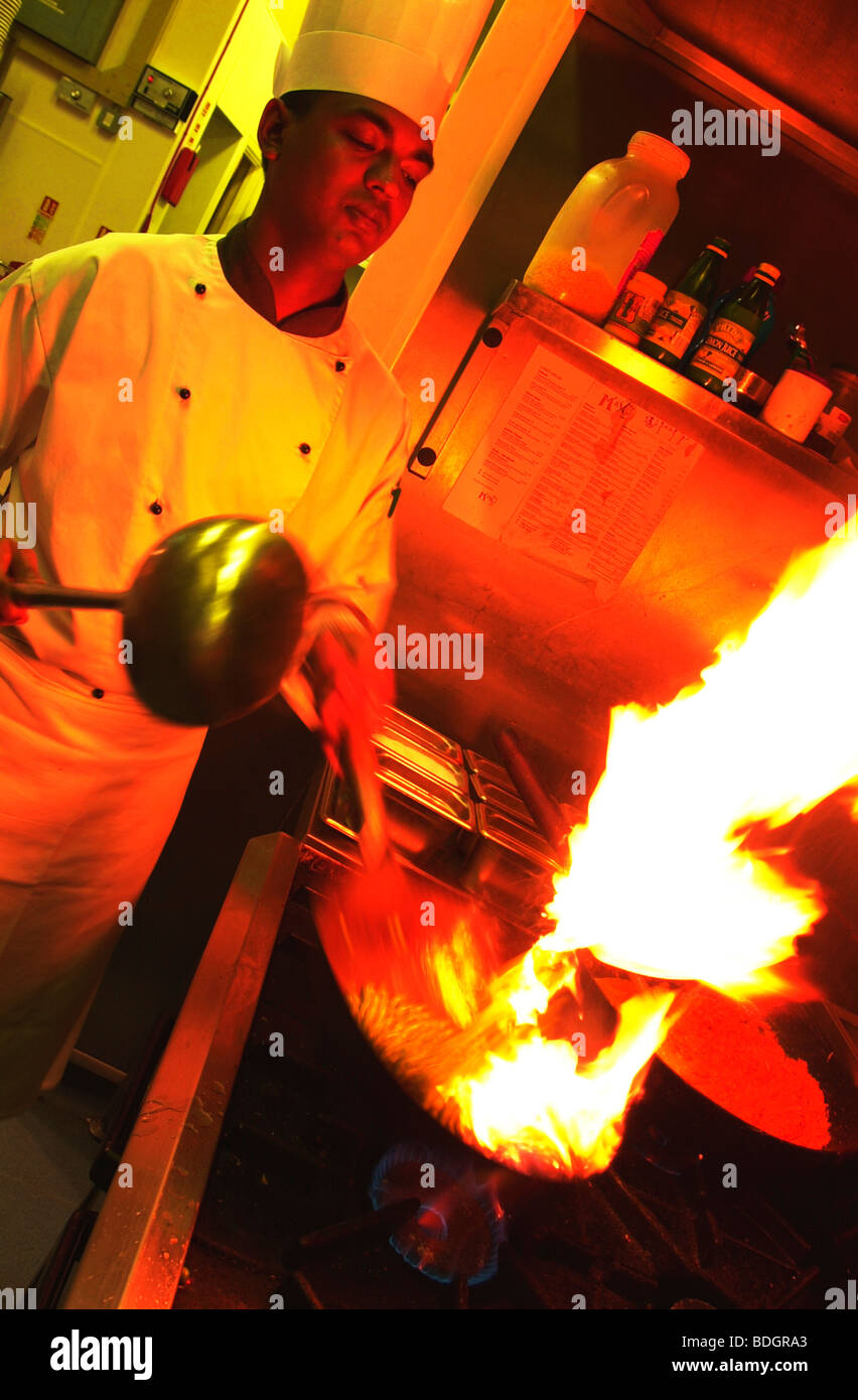 Chef indiano indossando bianchi e il cappello da cuoco di colore rosso fiamma di cottura stufa flambe antincendio Foto Stock