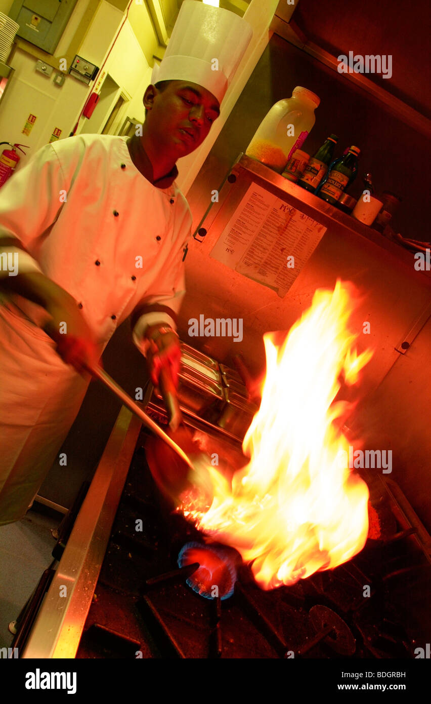Chef indiano indossando bianchi e il cappello da cuoco di colore rosso fiamma di cottura stufa flambe antincendio Foto Stock