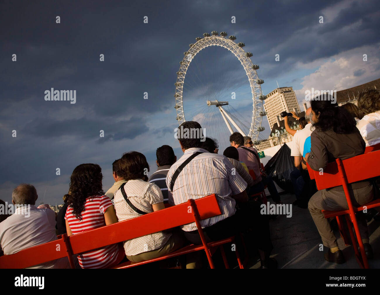 I turisti in una crociera sul fiume in barca sul fiume Thame London di fronte a London Eye nuvoloso meteo serata estiva prima del tramonto Foto Stock
