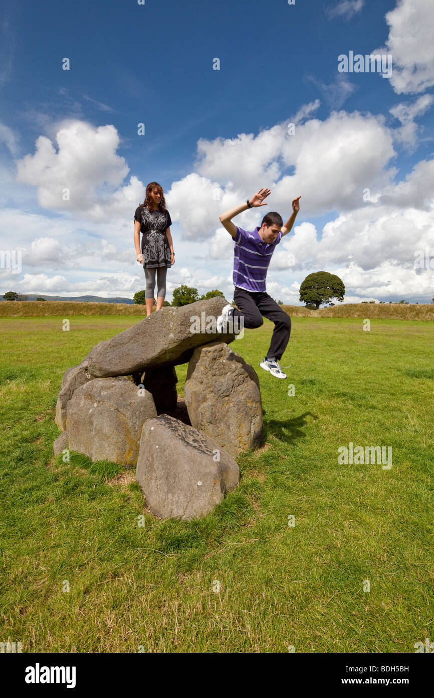Boy jumping girl permanente sulla sommità del dolmen al Giant's Ring, Lagan Valley, Belfast, Irlanda del Nord Foto Stock