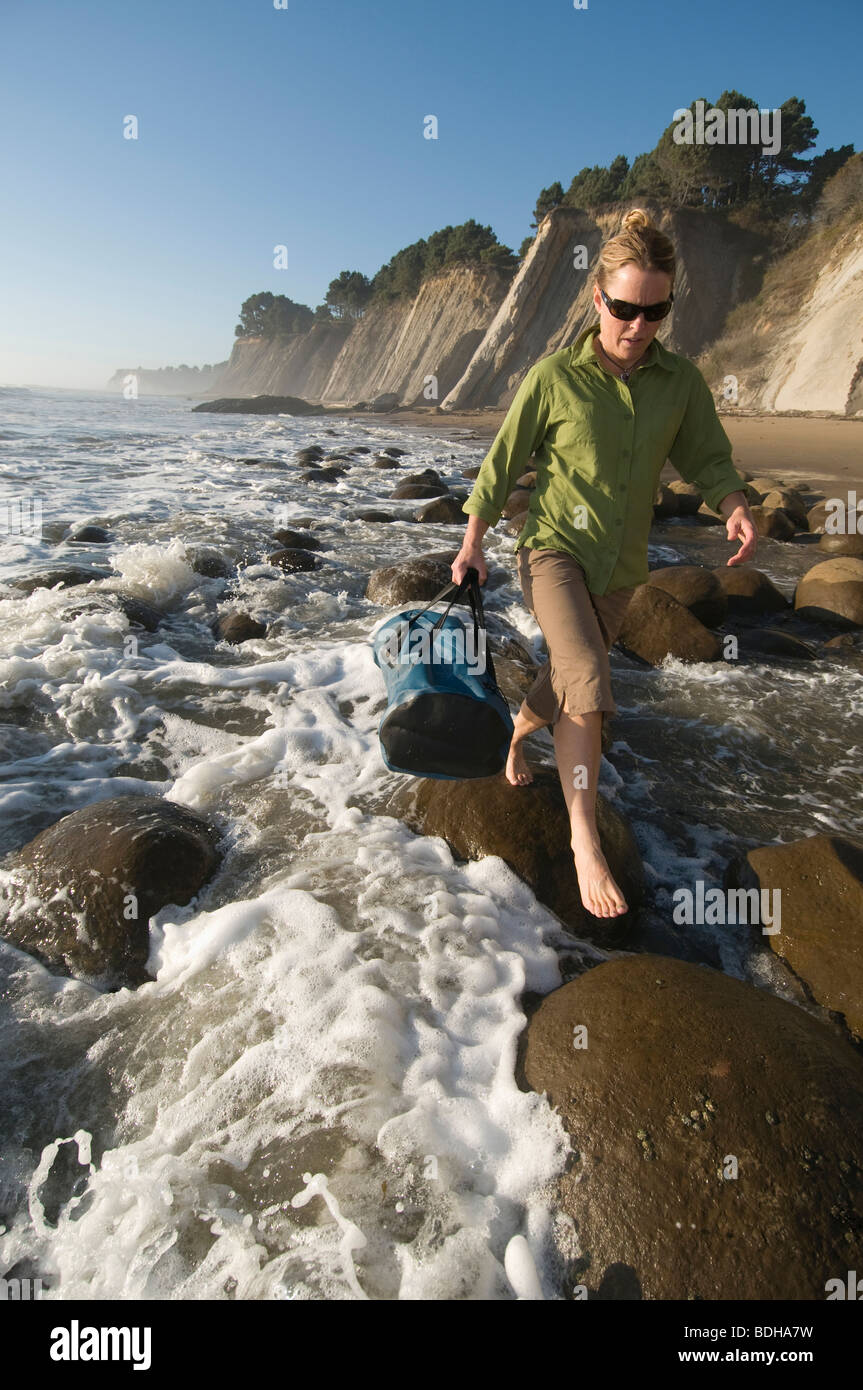 Una donna intensificazione su rocce rotonde nell'oceano surf vicino, punto Arena, California. Foto Stock