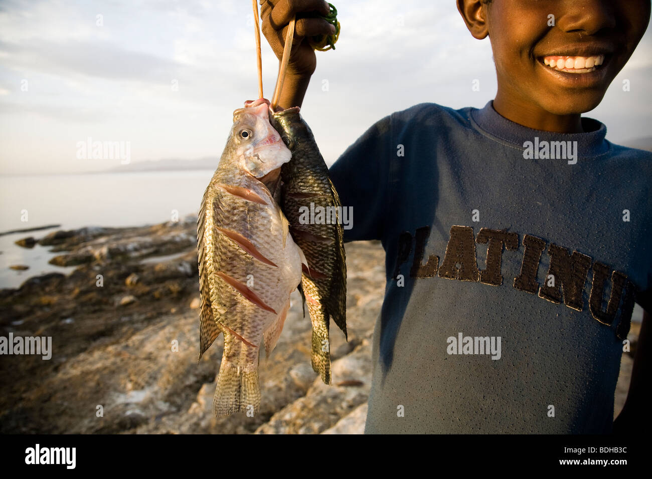 Un ragazzo sorride mentre si tiene una stringa di pesce pescato in corrispondenza del bordo di un lago. Foto Stock