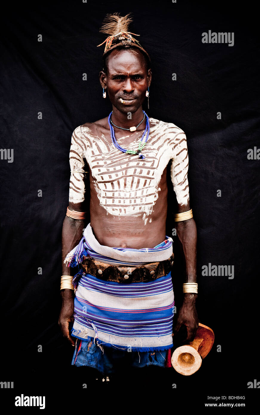 Ritratto di un uomo in abito tradizionale e decorazione del corpo poste prima di un panno nero. Foto Stock