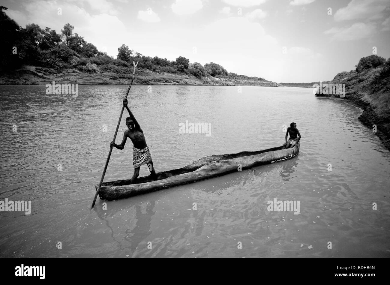 Un povero ragazzo nero in abito tradizionale poli una piroga attraverso una lenta, ampio fiume con un altro ragazzo in prua. Foto Stock