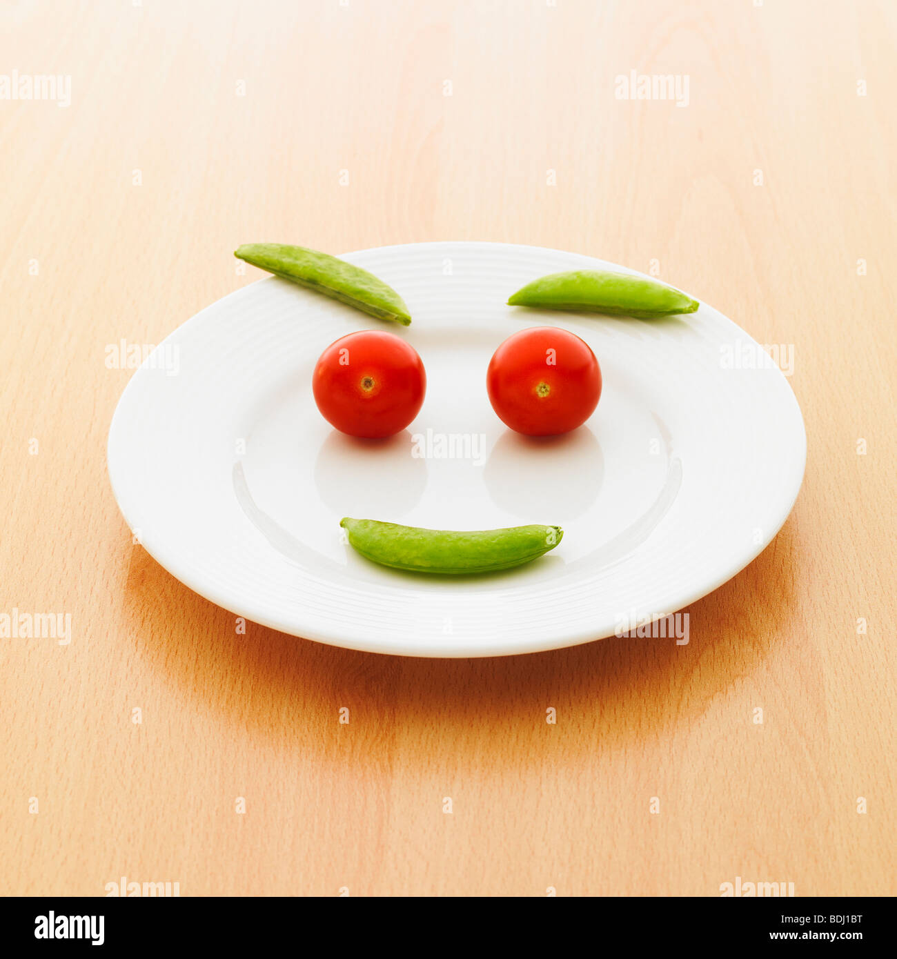 Una piastra di pomodori ciliegia e zucchero piselli a scatto facendo una faccina sorridente. Foto Stock
