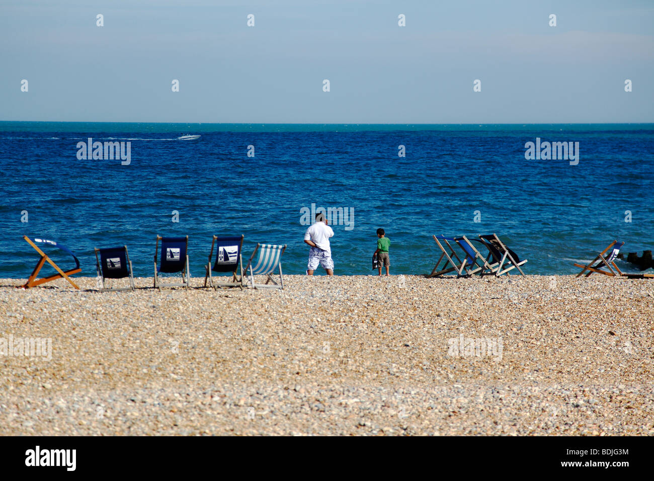 Inghilterra, East Sussex, Eastbourne, uomo e ragazzo sulla spiaggia con sedie a sdraio al vento. Barca veloce passando da Foto Stock