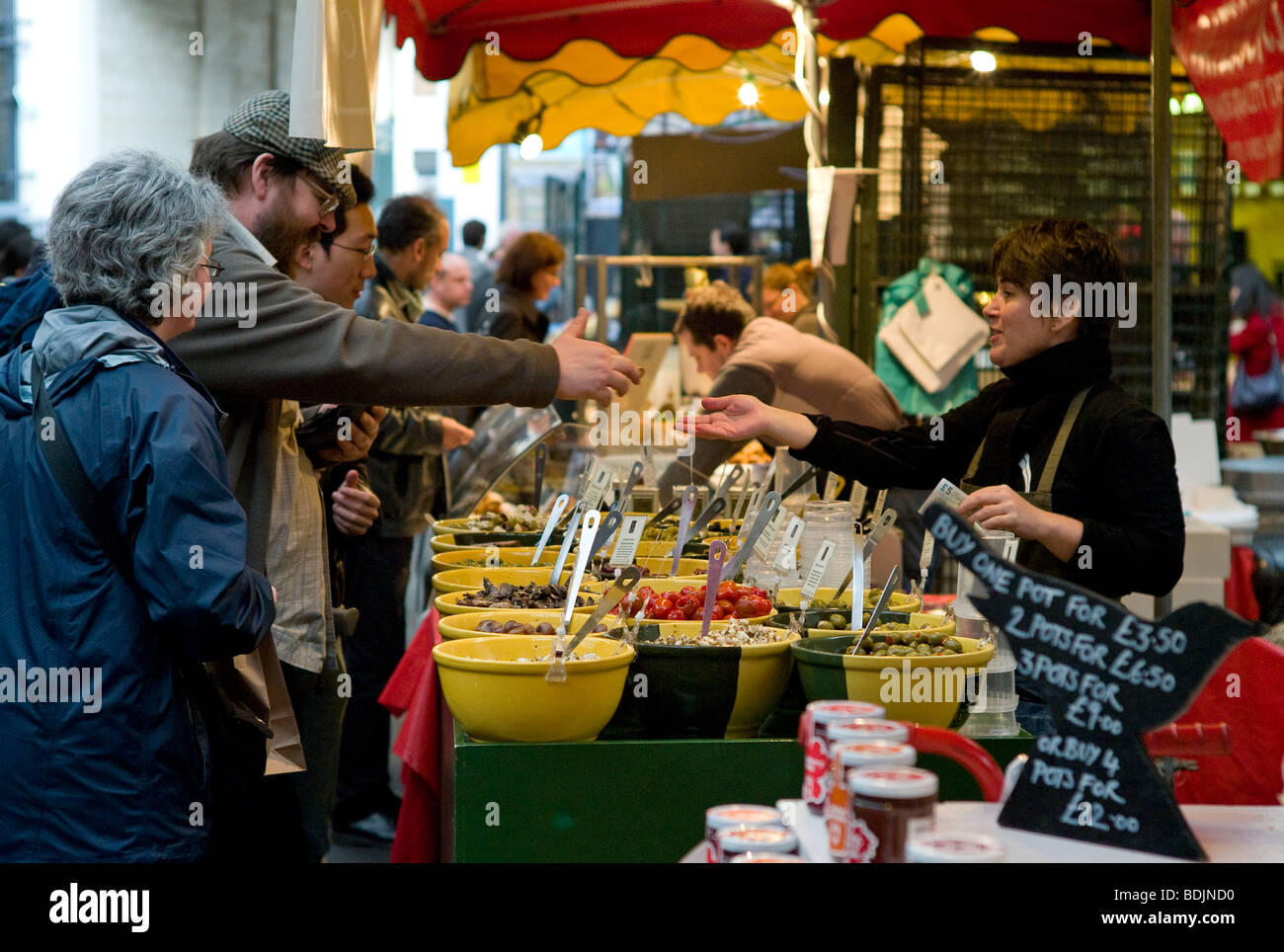 I clienti che acquistano olive fresche dal commerciante in stallo, Borough Market, Londra Foto Stock