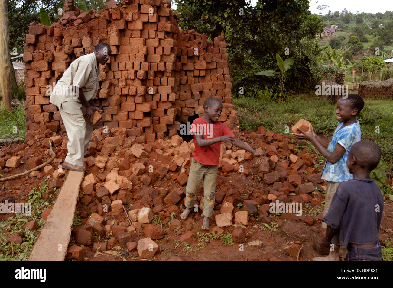 Un uomo e tre bambini lavorano insieme per stack e annullare la disposizione in pila di mattoni per la costruzione di una casa in Uganda east africa africa Foto Stock
