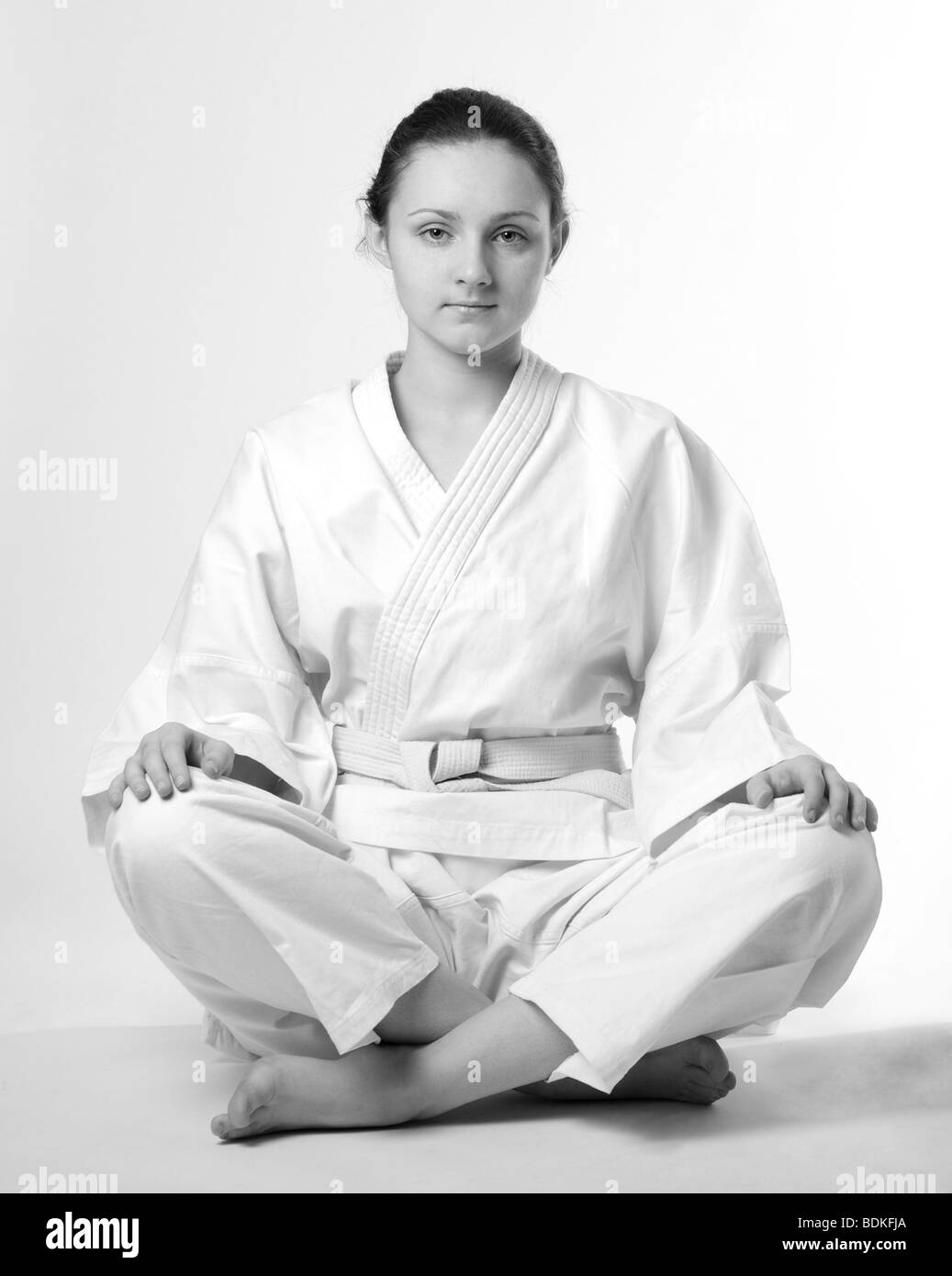 Ragazza in bianco uniforme seduto in posa tradizionali, sfumature di grigio, calma guardare Foto Stock