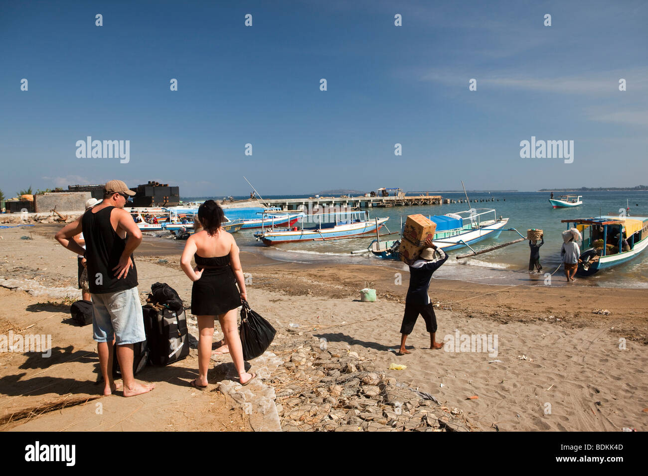 Indonesia, Lombok, Bangsal harbour persone che trasportano le scatole di acqua per piccole Gili Air public ferry boat come turisti attendere a terra Foto Stock