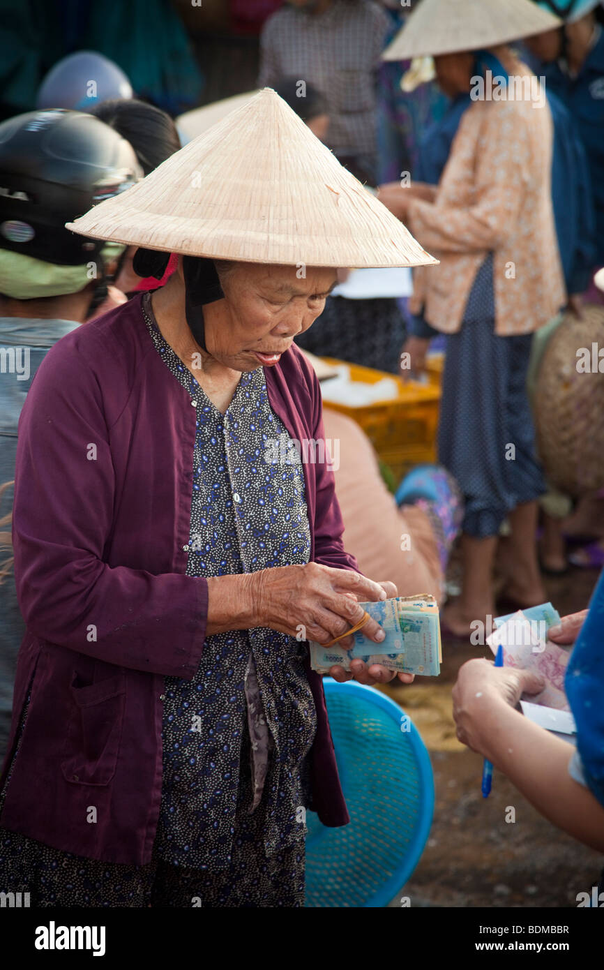 Un vietnamita vecchia donna lo scambio di denaro al mercato indossando un cappello conico Foto Stock