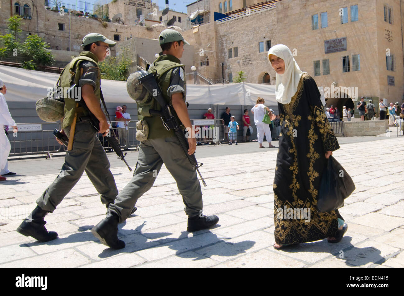 Soldati israeliani pattugliano la Città Vecchia di Gerusalemme si incrociano con un anziano velata donna palestinese. Foto Stock
