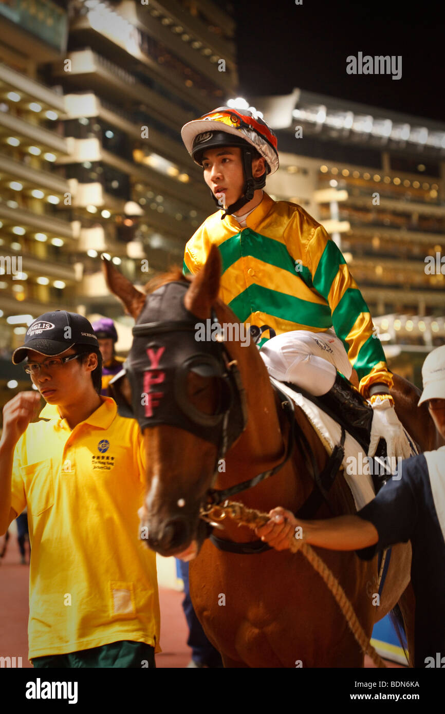 Un fantino sul suo supporto con il gestore nella parade ring in una notte horse racing event a Happy Valley Race Course a Hong Kong. Foto Stock