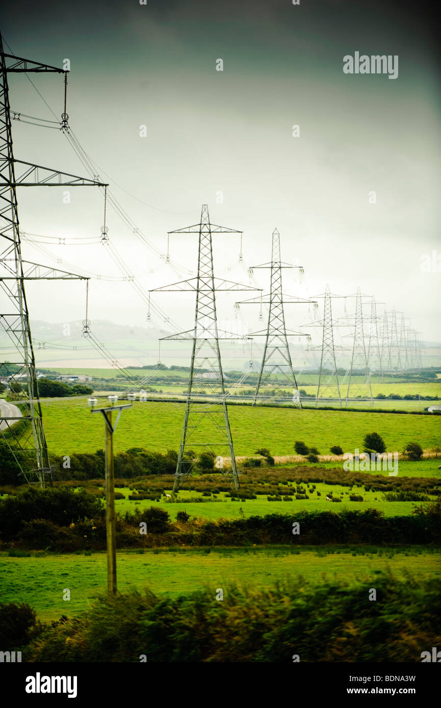 Una linea di riga della griglia nazionale di elettricità tralicci marciando attraverso il paesaggio rurale di Anglesey, Galles del Nord Regno Unito Foto Stock