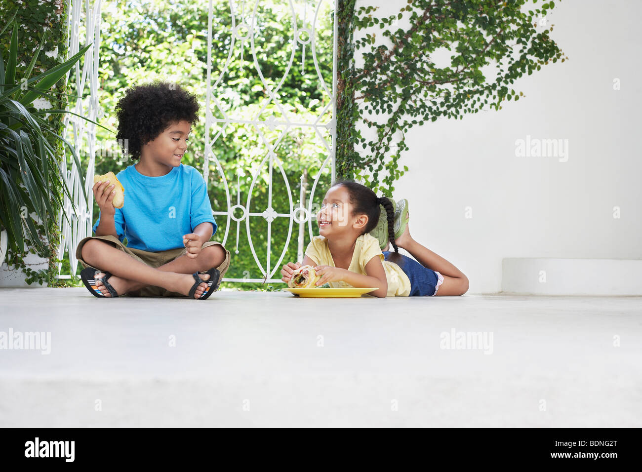 Un ragazzo e una ragazza (5-6 anni) mangiare sulla veranda piano Foto Stock