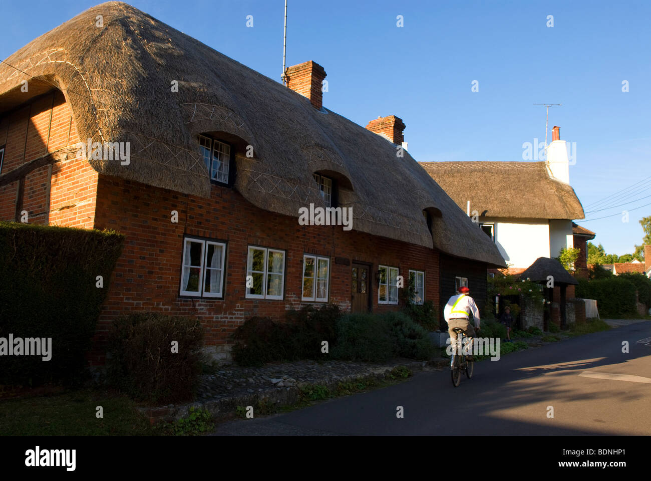 Un uomo che cavalca la sua bicicletta fino alla strada nel pittoresco villaggio di Hampshire di Selborne, Hampshire REGNO UNITO. Foto Stock