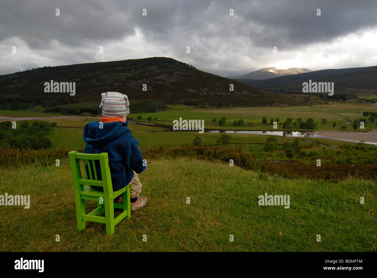 Giovane ragazza seduta su una sedia verde, guardando le Highlands scozzesi, fiume e foreste, Scozia, Europa Foto Stock