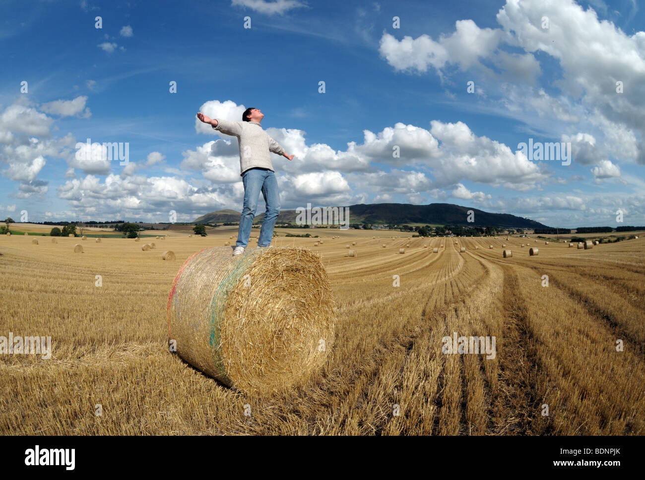 Un giovane ragazzo in un campo con balle di fieno con le braccia aperte. Foto Stock