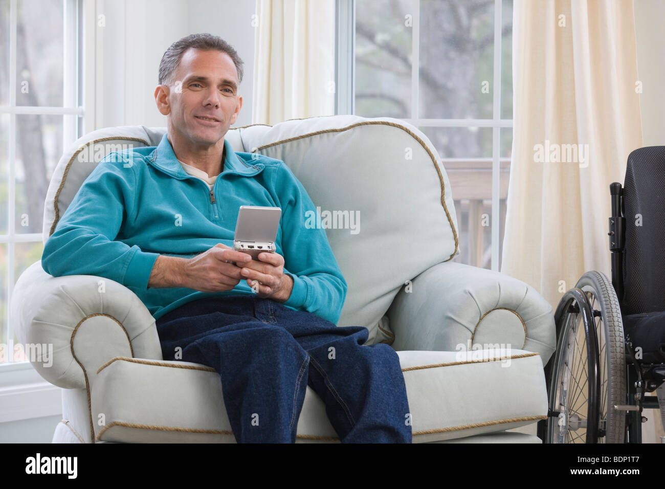 Uomo seduto in una sedia a rotelle e tenendo un assistente di dati personale Foto Stock