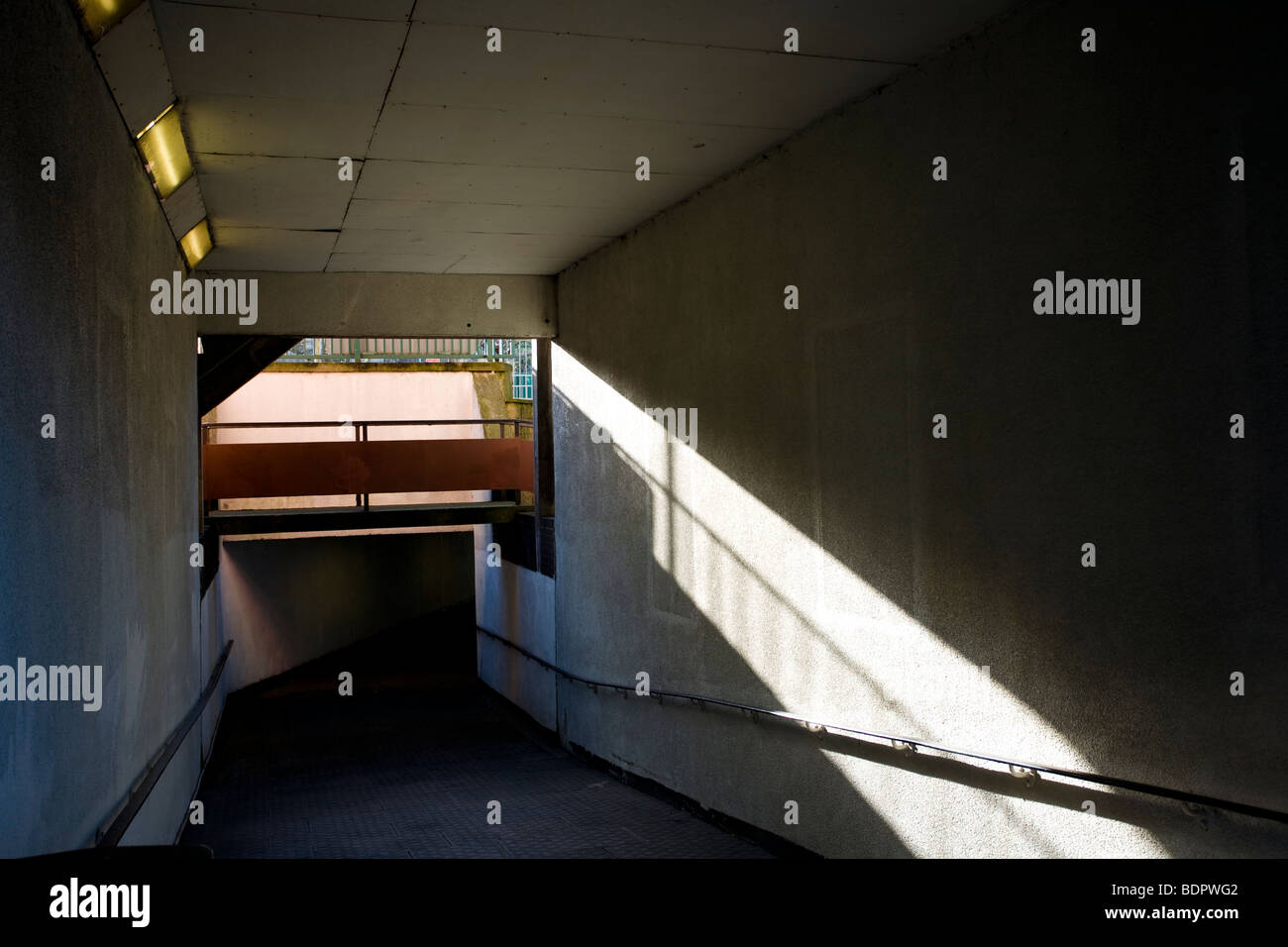 Luce e ombra in un sottopassaggio urbano in cemento. Un passaggio duro che mostra forme geometriche, forti linee angolari e un senso di isolamento. Foto Stock