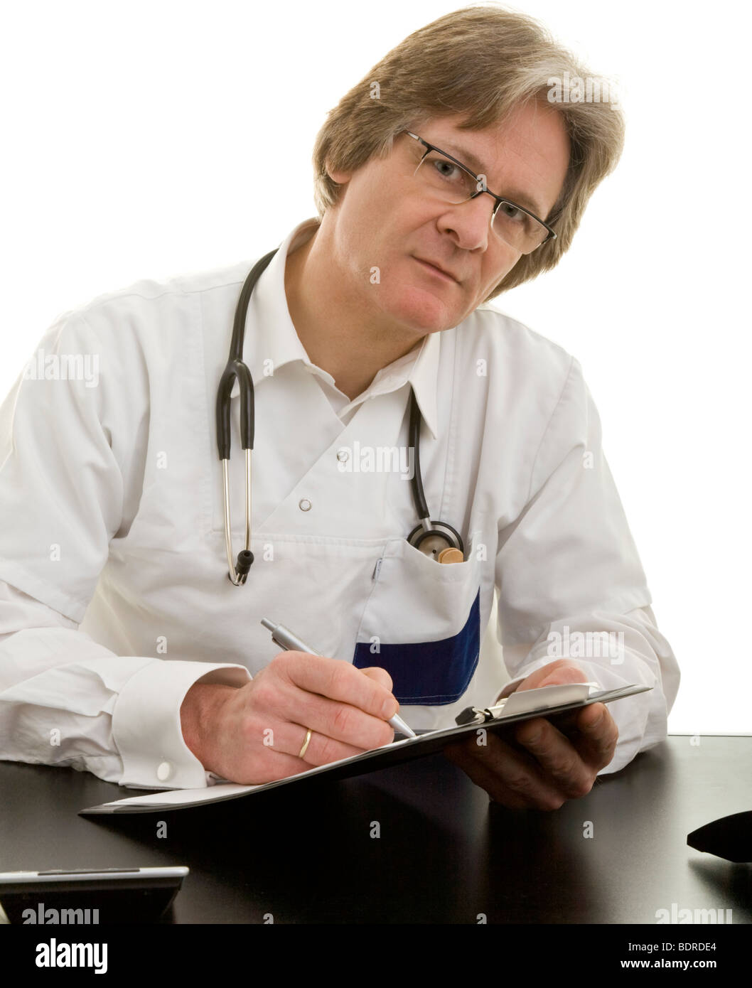 Arzt sitzt mit Kugelschreiber und Klemmbrett un seinem Schreibtisch Foto Stock