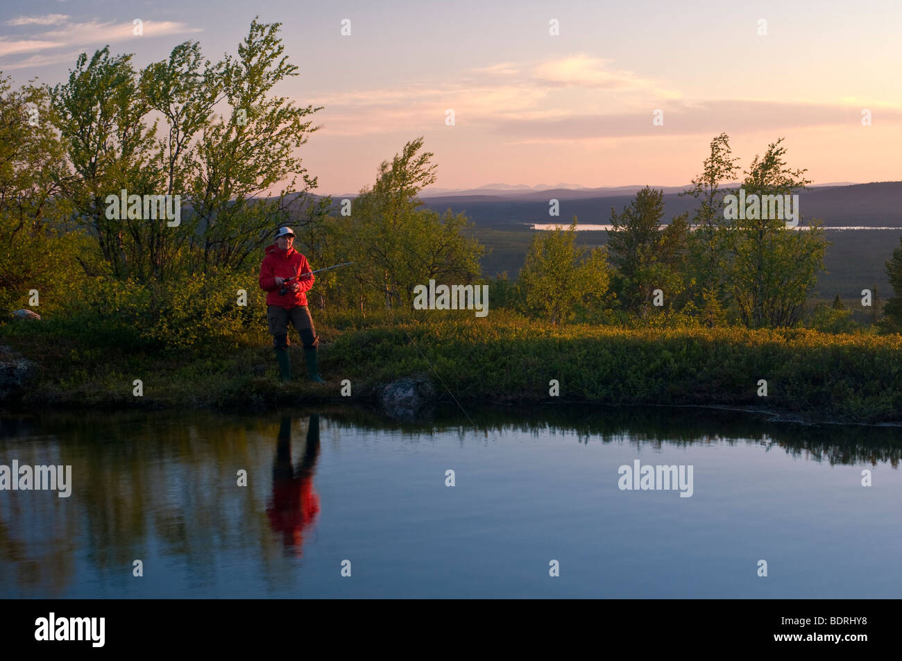 Pescatore femmina in corrispondenza di un lago di montagna in Lapponia al sole di mezzanotte, Svezia Foto Stock