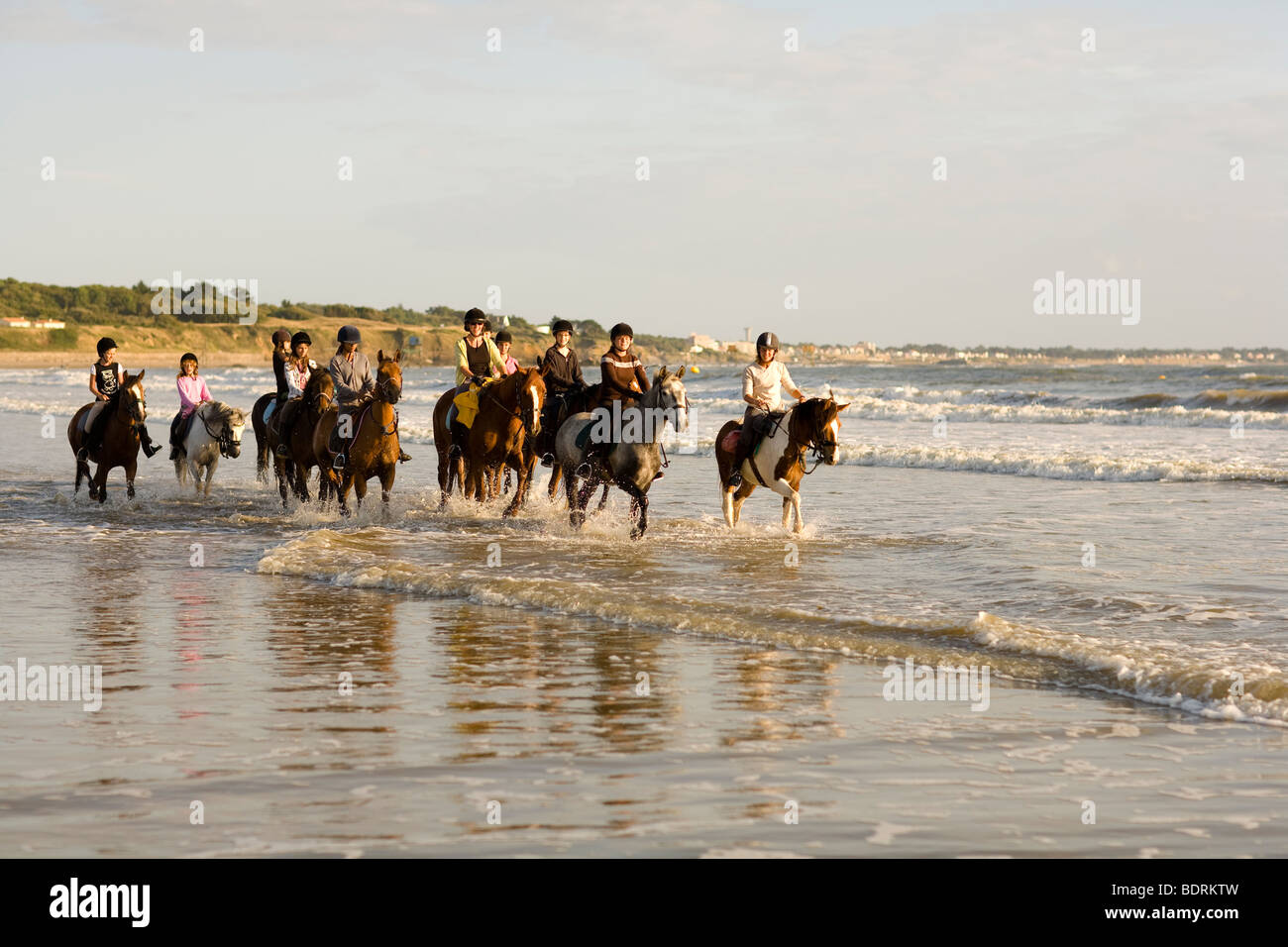 Un maneggio con scuola di equitazione passa per un hack in spiaggia e il surf. I piloti sono di tutte le diverse età e capacità. Foto Stock