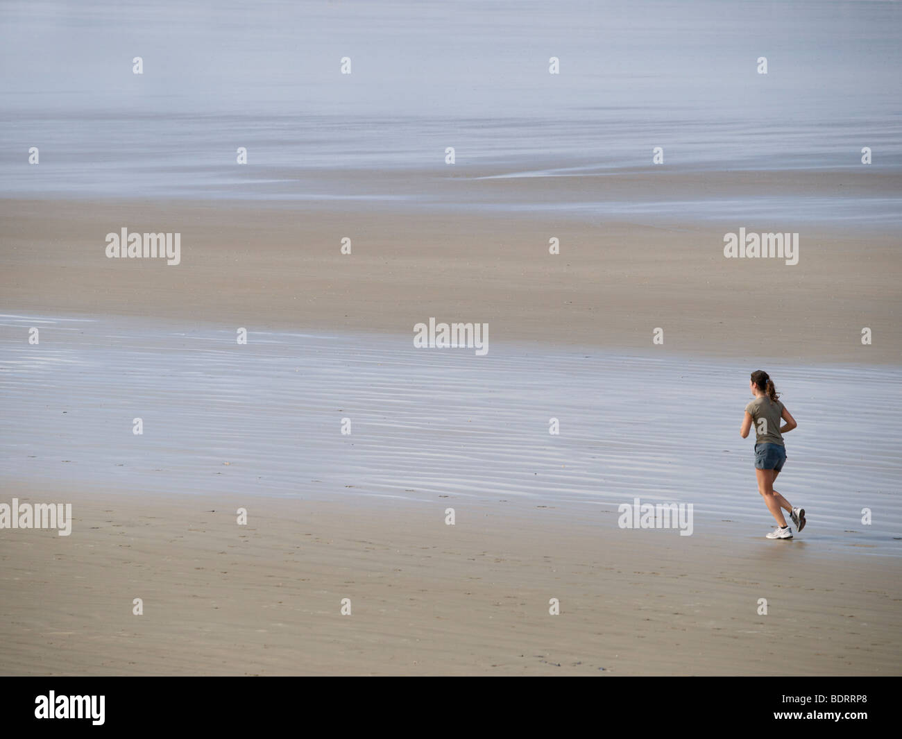 Donna jogging sulla spiaggia di San Nic, Brittany, Francia Foto Stock