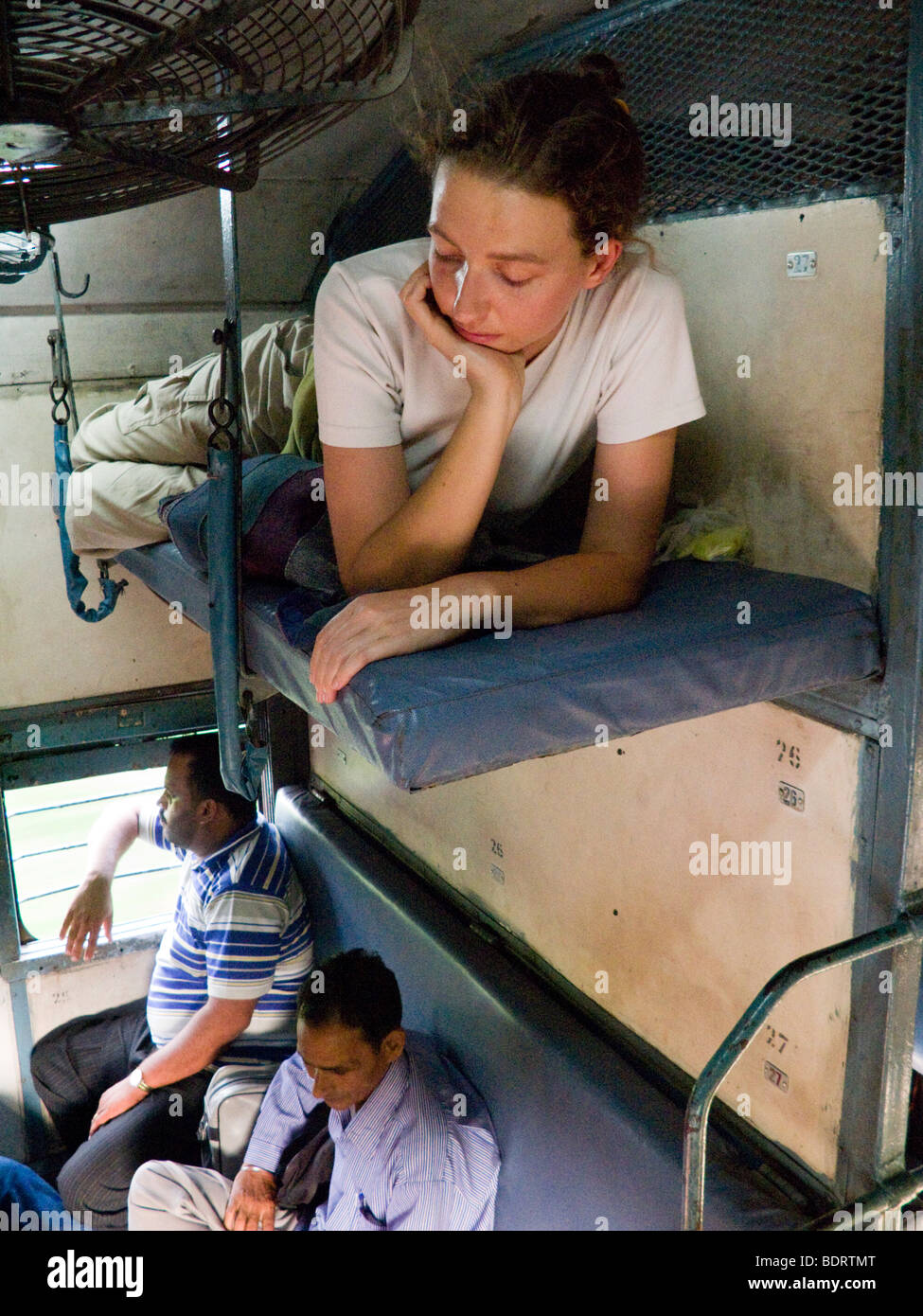 Western European Passenger in appoggio su un letto Sleeper, Indiano sopra i passeggeri seduti in una traversina vano. Treno indiano. Foto Stock