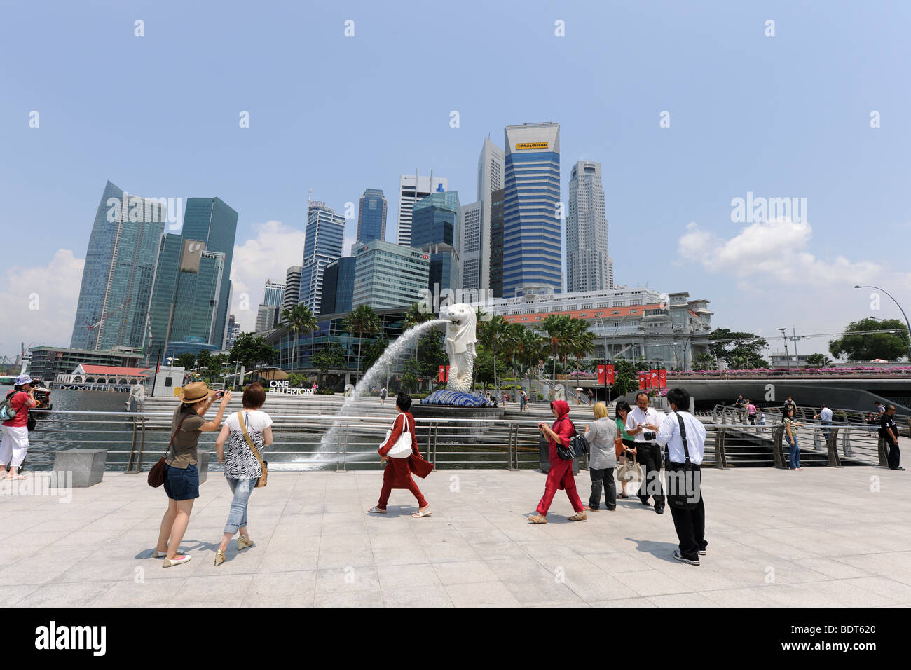 I turisti scattano fotografie di fronte al Merlion con lo skyline della citta' dietro, Singapore Foto Stock
