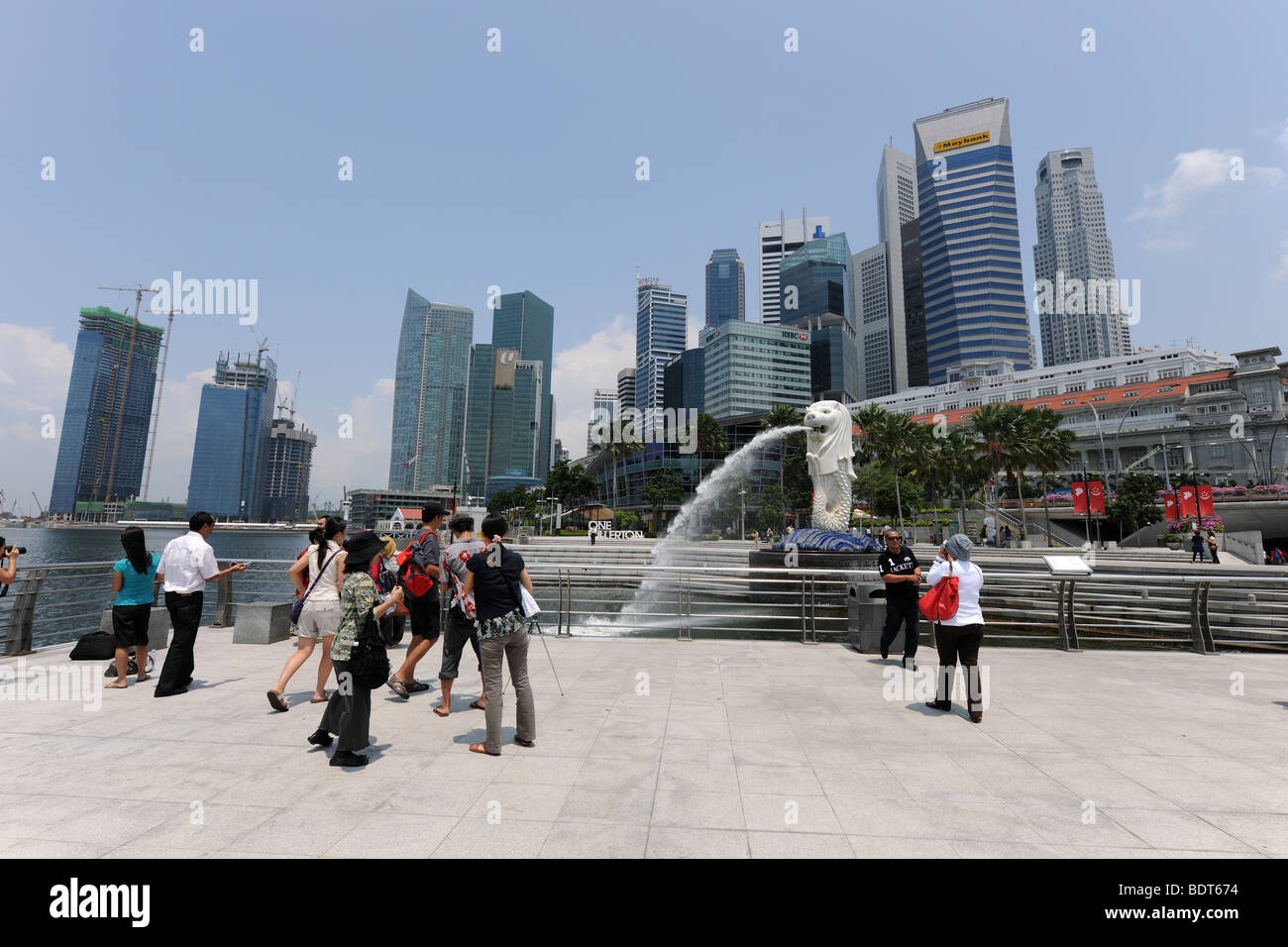 I turisti scattano fotografie di fronte al Merlion con lo skyline della citta' dietro, Singapore Foto Stock