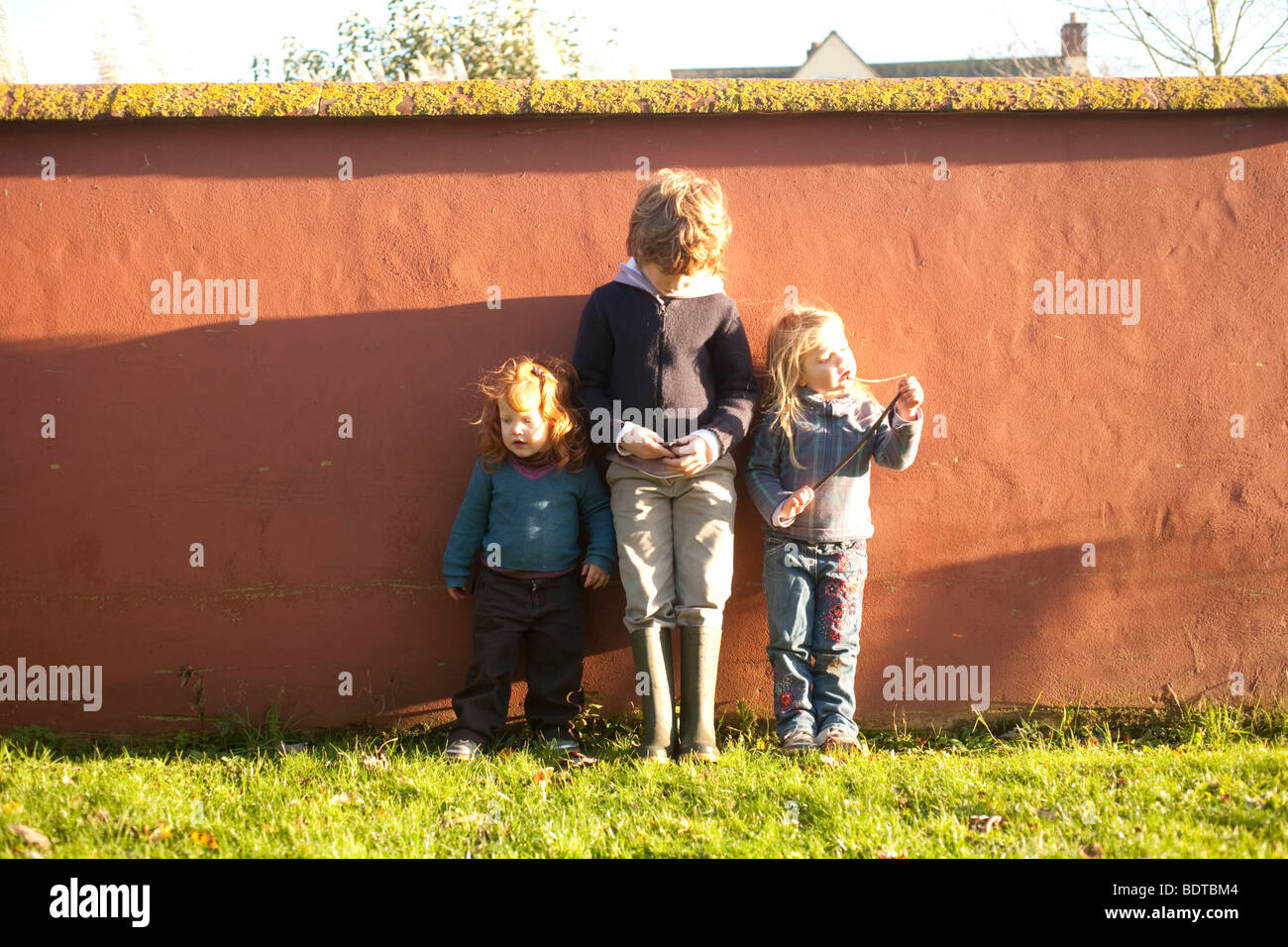 Fratelli e due sorelle più giovani in piedi contro un muro in presenza di luce solare Foto Stock