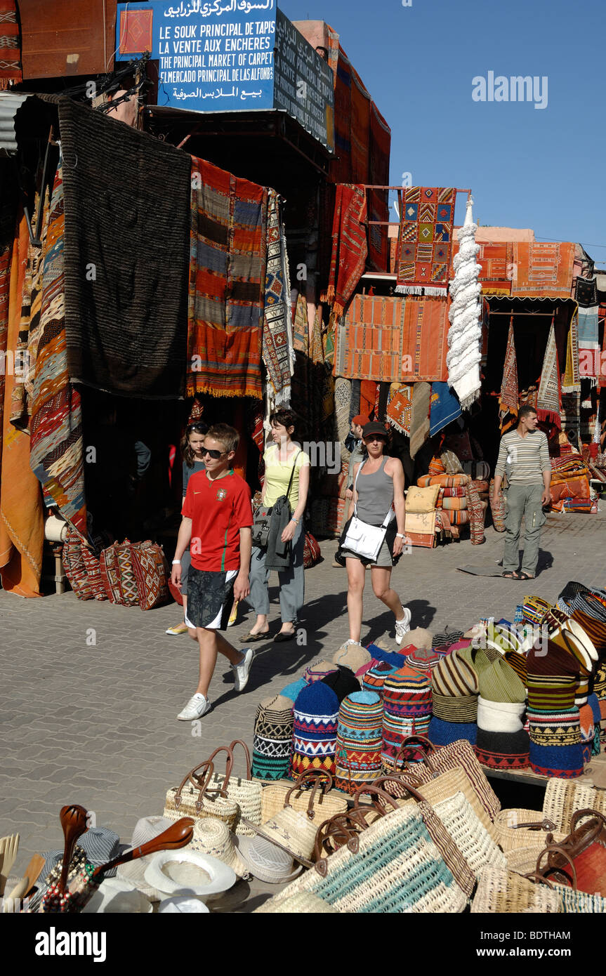 Giovani turisti occidentali a piedi attraverso il tappeto Bazaar, mercato o souk, Place aux Epices, Marrakech, Marocco Foto Stock