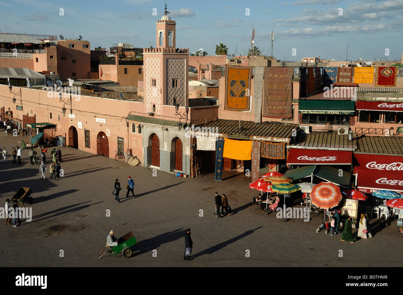 Serata in Djemaa El-Fná o Djemaa El Fna con minareto della moschea, & negozi di tappeti, Marrakech, Marocco Foto Stock