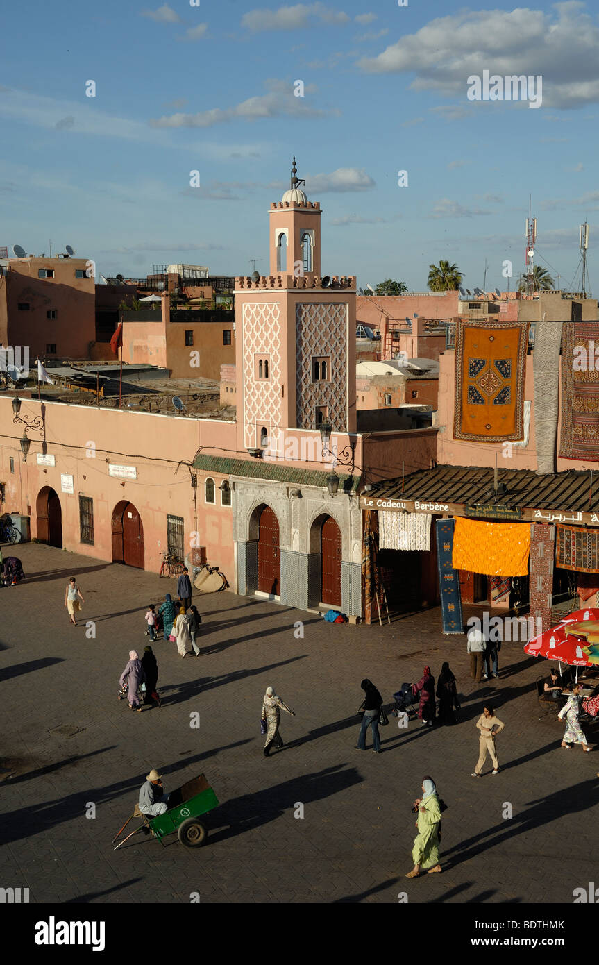 Di sera su Djemaa El-Fná o Djemaa El Fna con minareto e negozi di tappeti, Marrakech, Morooco Foto Stock