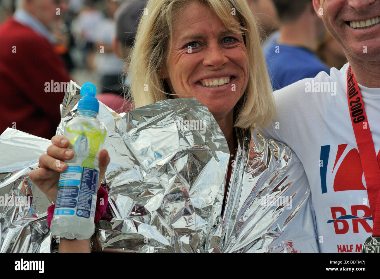 Giovane donna runner in lamina wrap azienda drink dopo Bristol mezza maratona, REGNO UNITO Foto Stock
