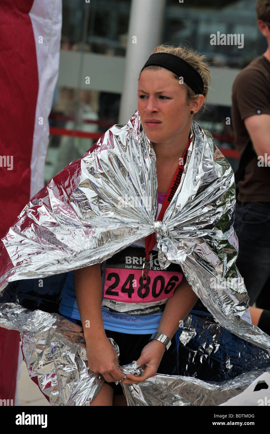 Giovane donna runner nel foglio di avvolgimento e di recupero a guardare gli altri corridori dopo Bristol mezza maratona, REGNO UNITO Foto Stock