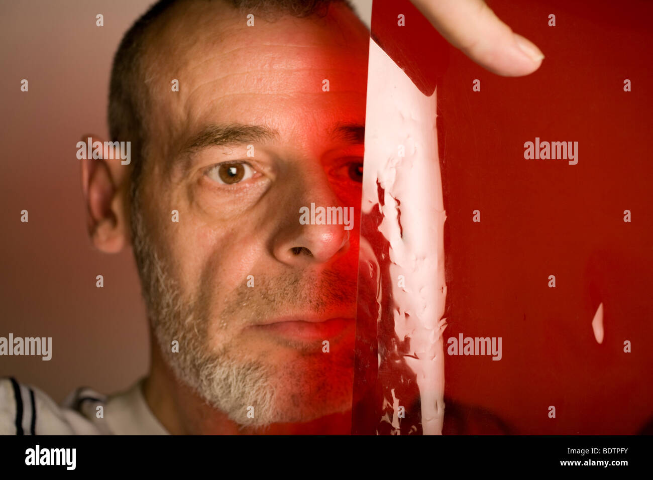 Un insolito, ma immagine artistica di un uomo guardando attraverso un gel rosso (acetato) foglio. Foto Stock