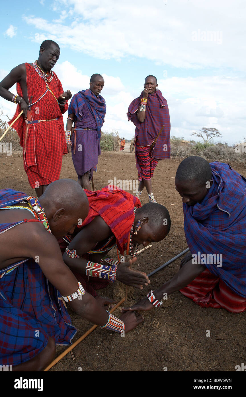 Kenia Masai uomini innescando un incendio nel modo tradizionale sfregando due bastoncini insieme e di accensione di asciugare sterco di elefante. Foto Stock