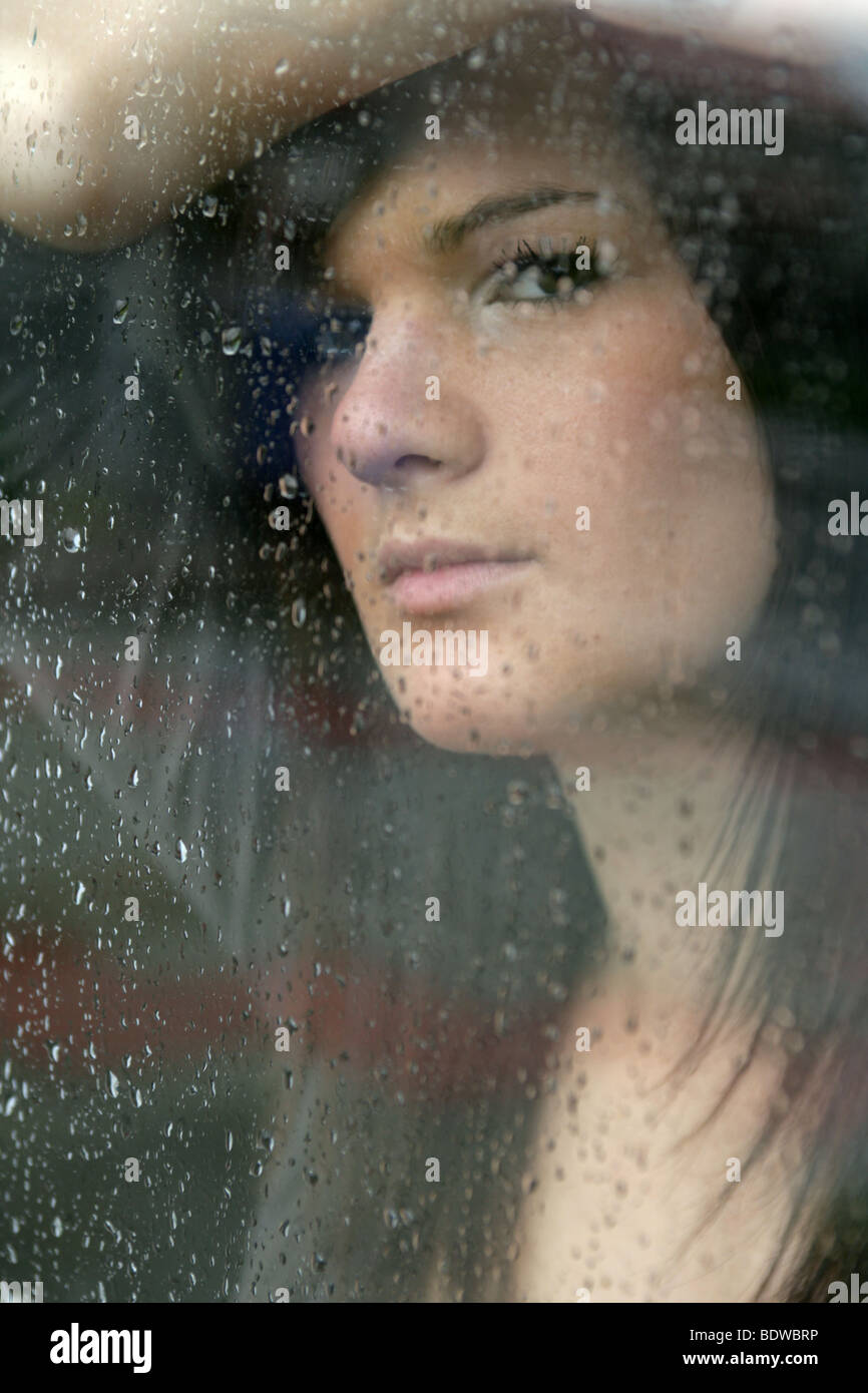 Dai capelli scuri donna che guarda fuori pioggia inzuppato finestra. Foto Stock