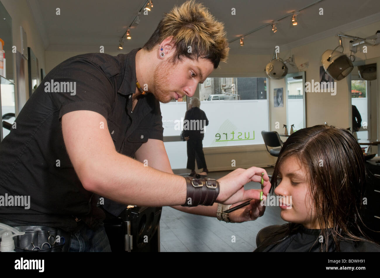 Un adolescente ottenendo il suo taglio di capelli da un parrucchiere in un salone di parrucchiere Foto Stock