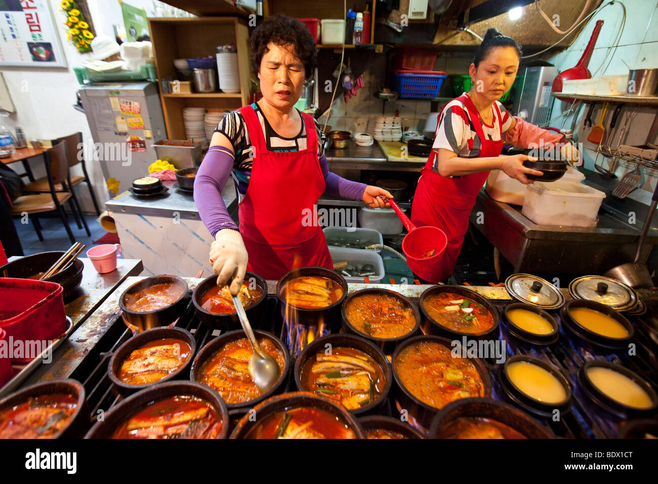 Donna di cottura jiggae piccante o stufato nel mercato Namdemun in Seoul COREA DEL SUD Foto Stock