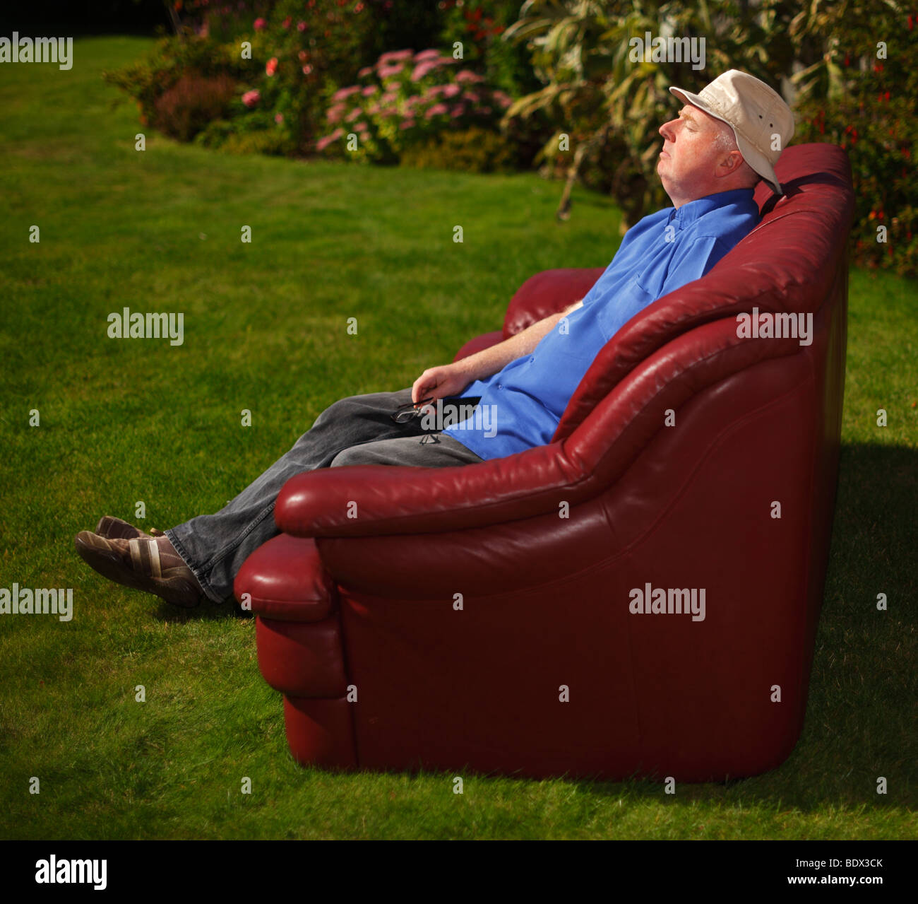 Uomo seduto in giardino su un divano. Foto Stock